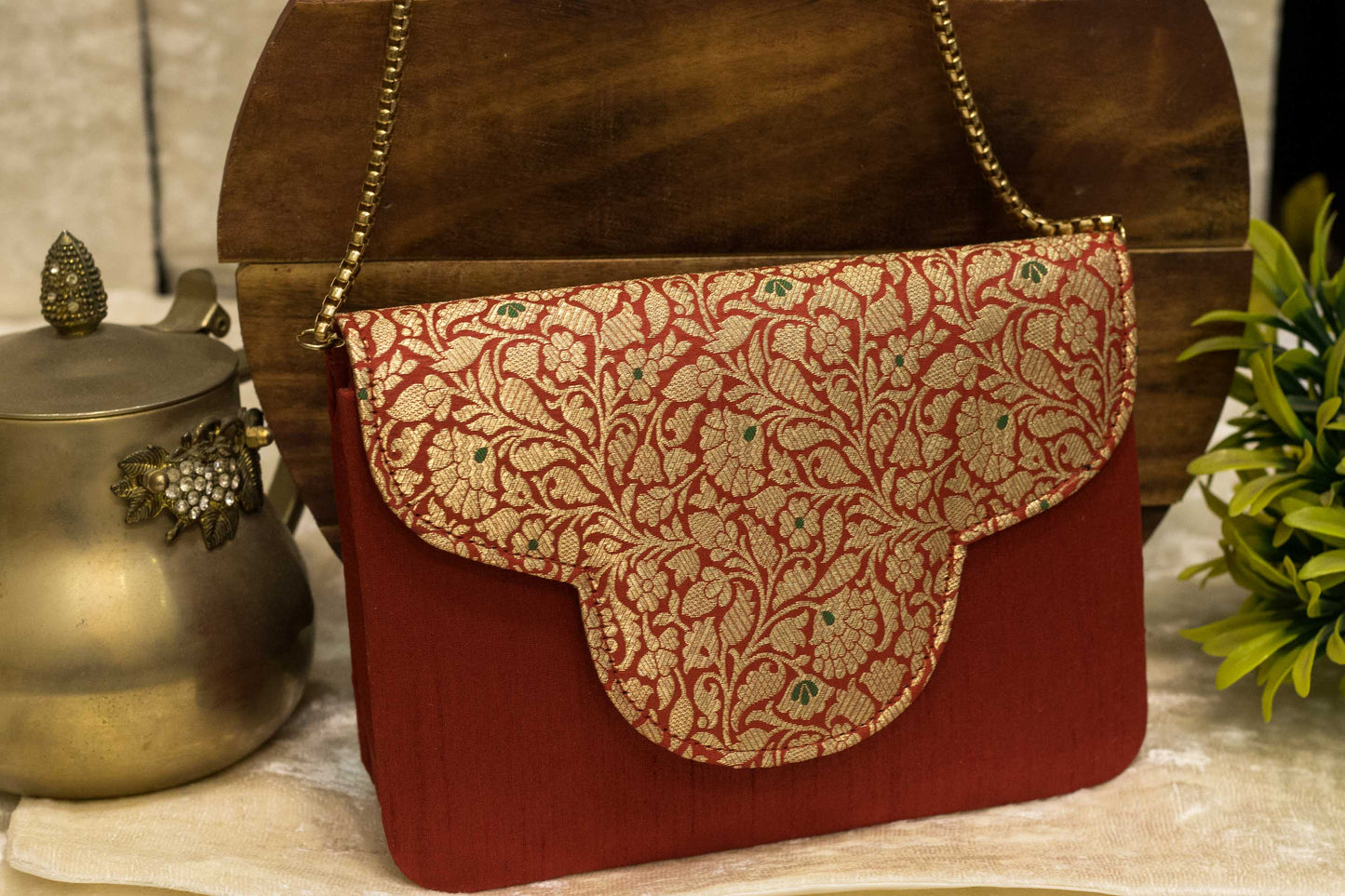 Red handmade traditional Banarasi brocade clutch bag with gold chain and intricate floral pattern.