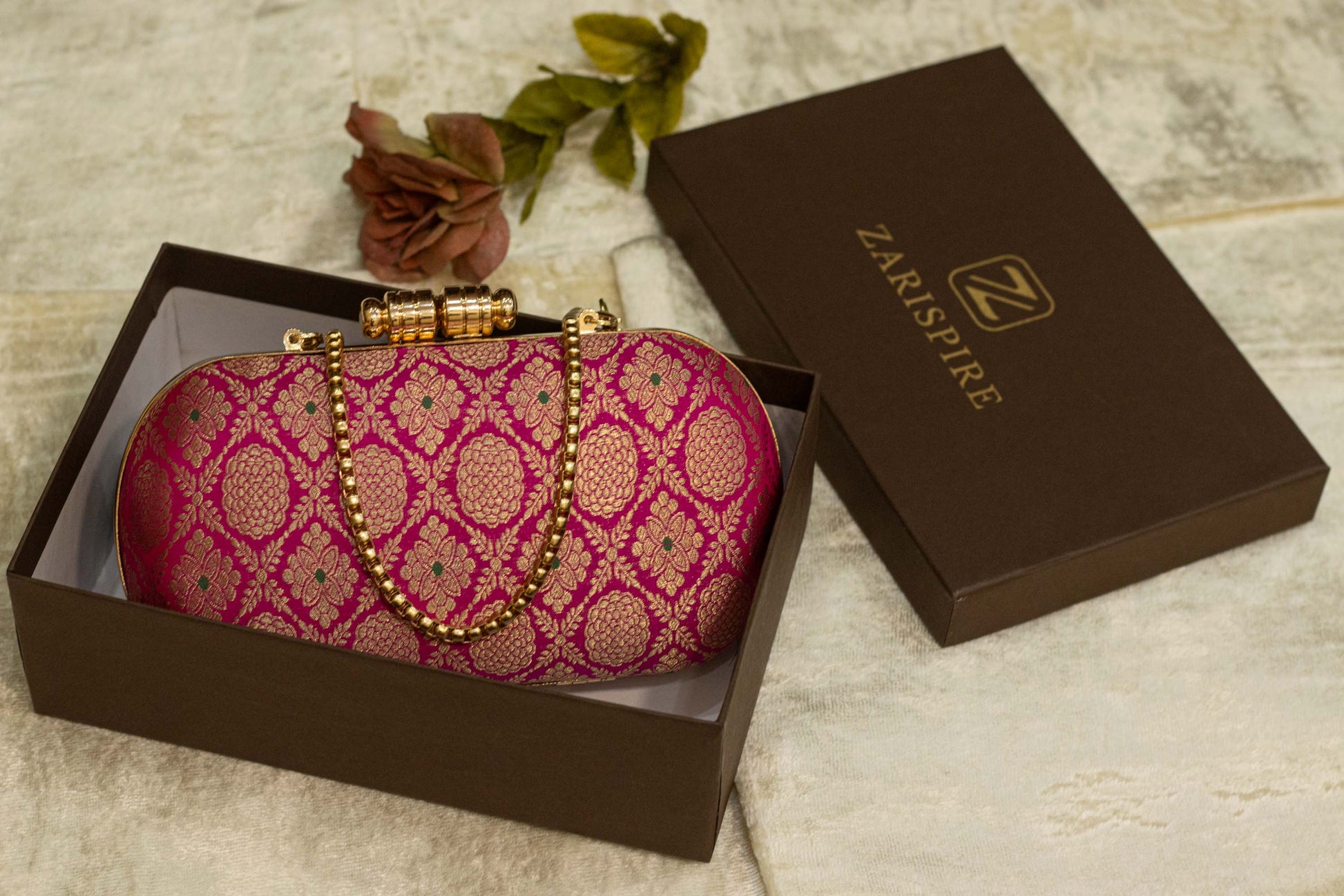 Rani pink Banarasi brocade clutch bag with traditional gold pattern and chain handle, handmade design.