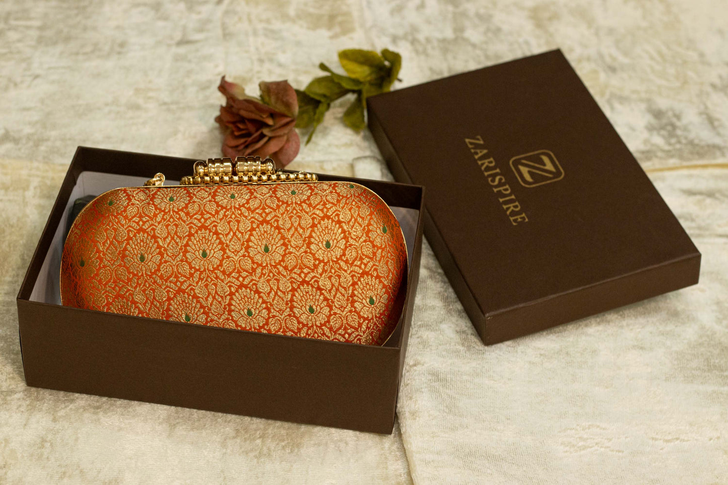 Saffron Banarasi brocade clutch bag with intricate traditional handmade patterns in a brown box.