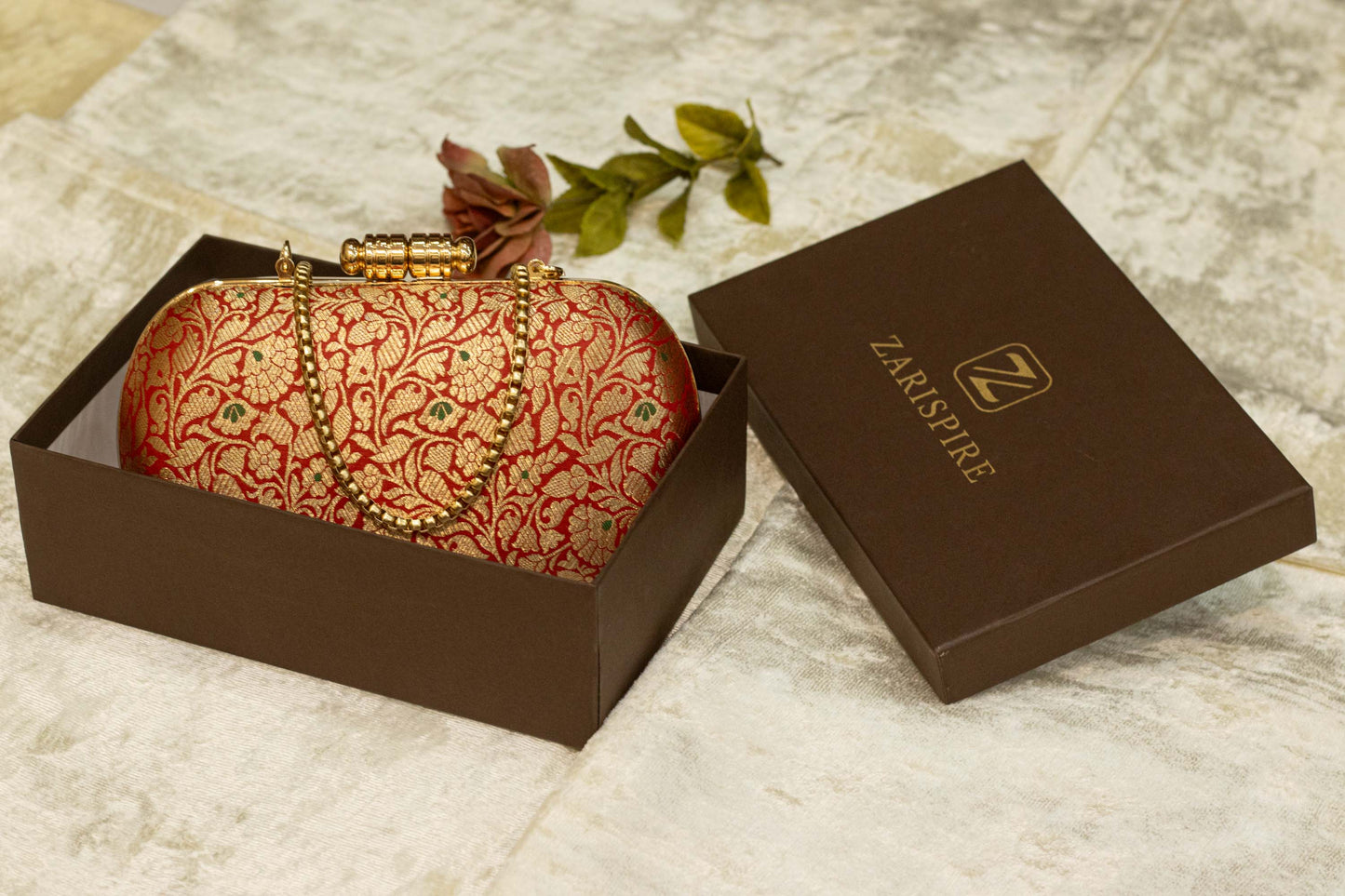 Red brocade Banarasi clutch bag with gold floral pattern, traditional handmade capsule clutch in a brown box.