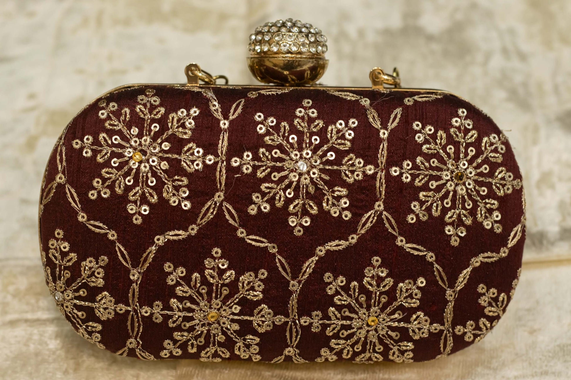 Maroon banarasi brocade clutch bag with gold floral embroidery and jeweled clasp, traditional handmade design.