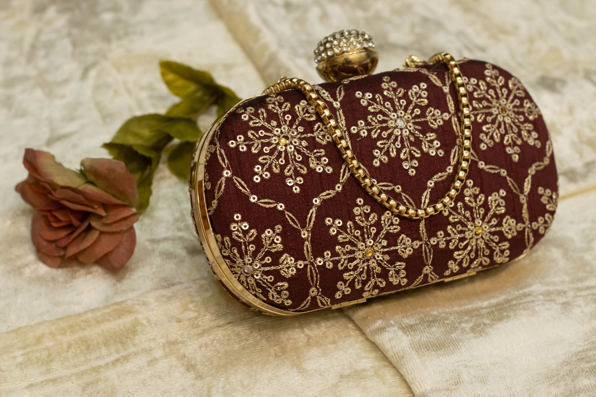 Maroon Banarasi brocade clutch bag with gold floral embroidery and decorative clasp, traditional handmade design.