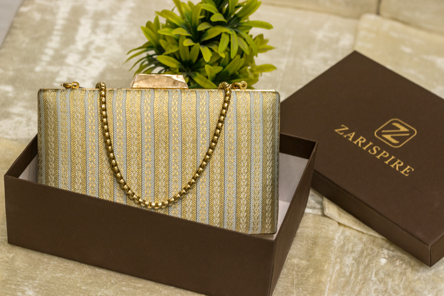 Sea blue Banarasi brocade clutch bag with gold chain, traditional handmade design in a brown box.