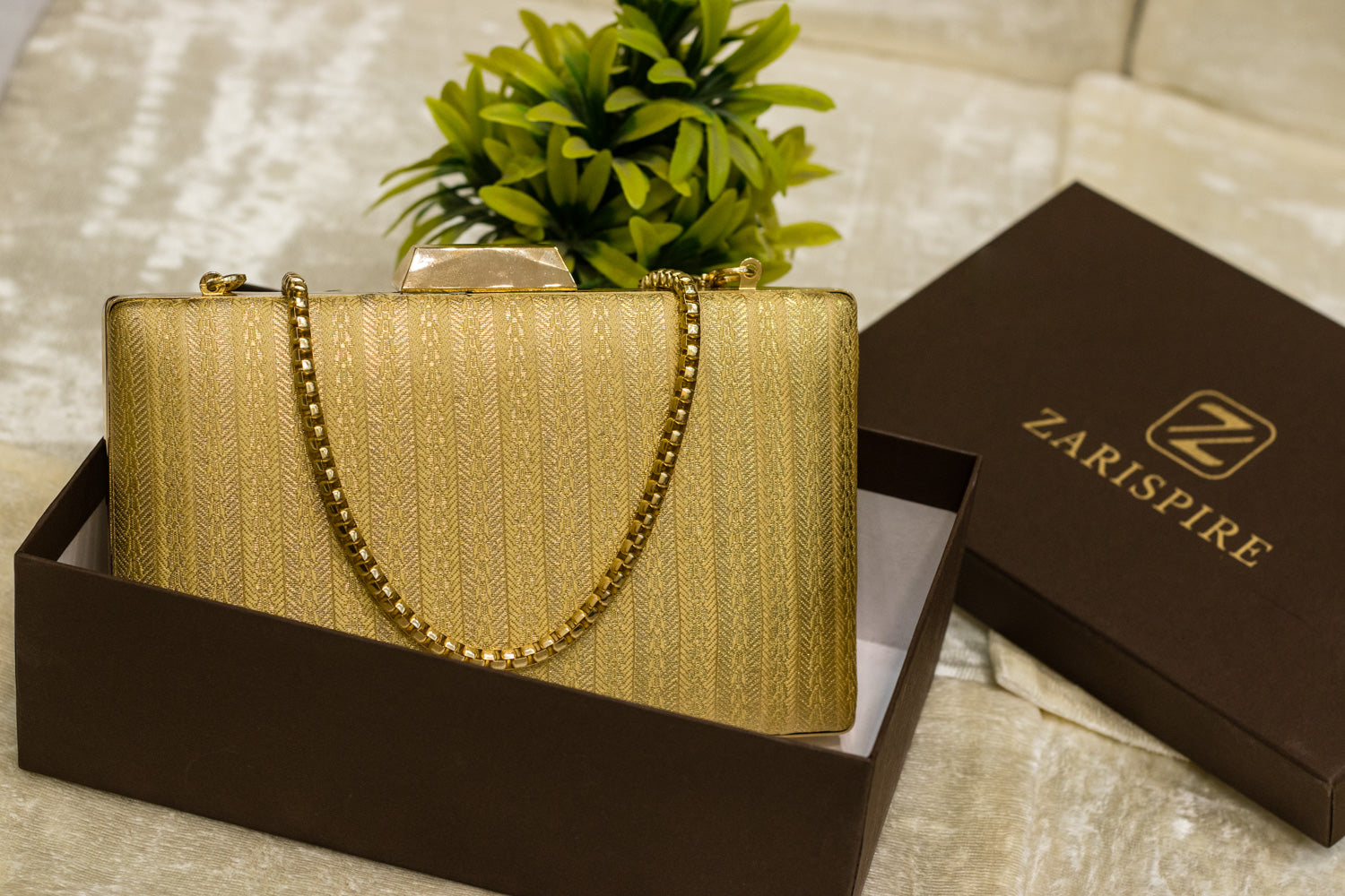 Beige Banarasi brocade clutch bag with gold chain, traditional handmade design in a black box.
