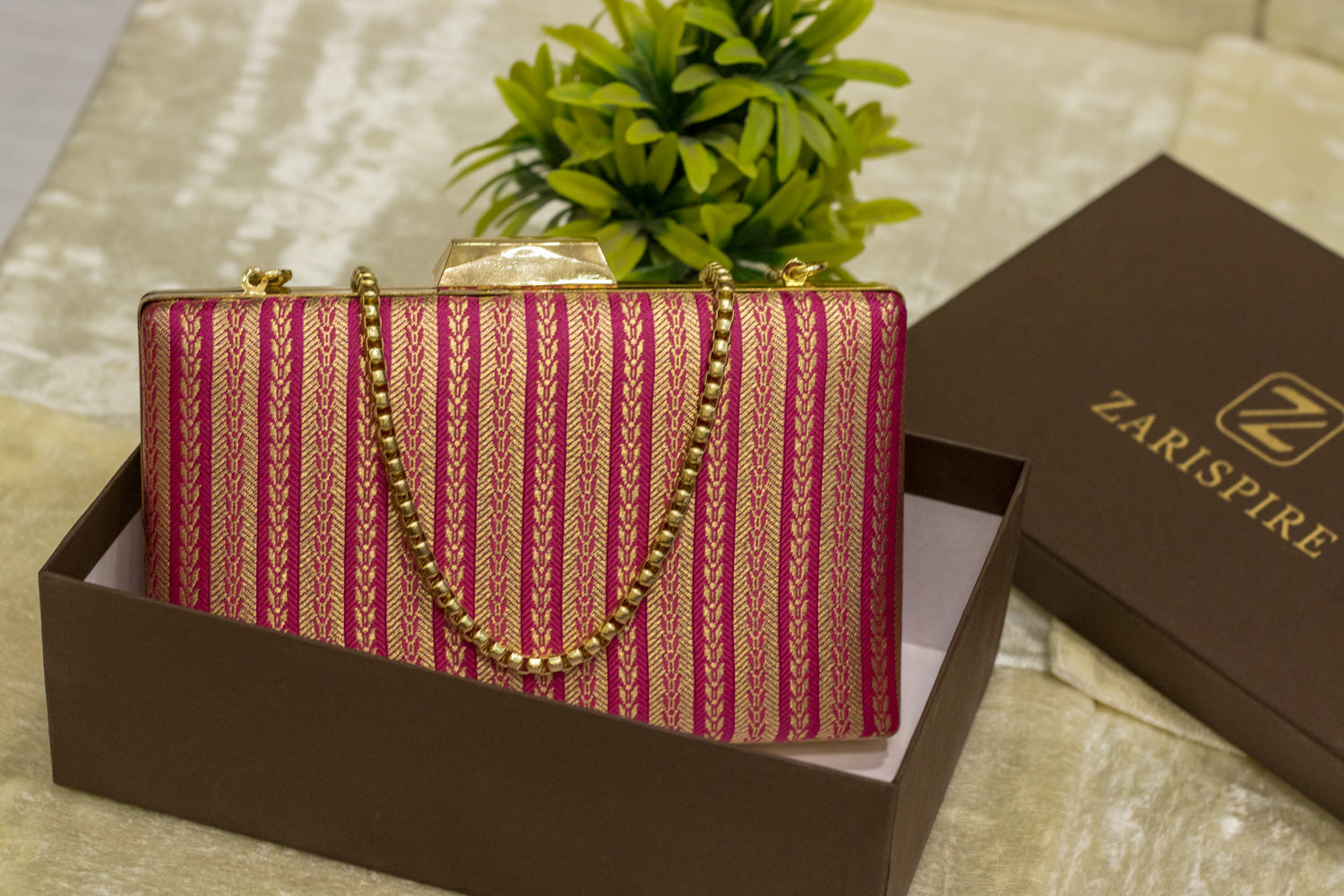 Rani pink brocade Banarasi clutch bag with gold chain, traditional handmade design in box.