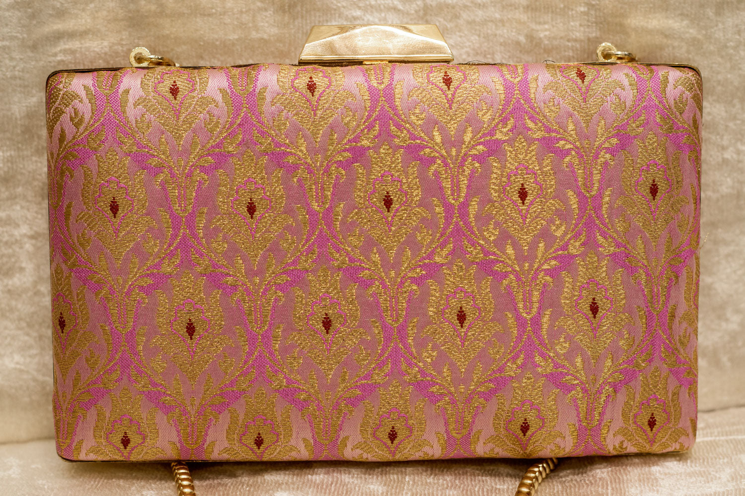 Pink Banarasi brocade clutch bag with traditional handmade gold patterns and a gold chain strap.