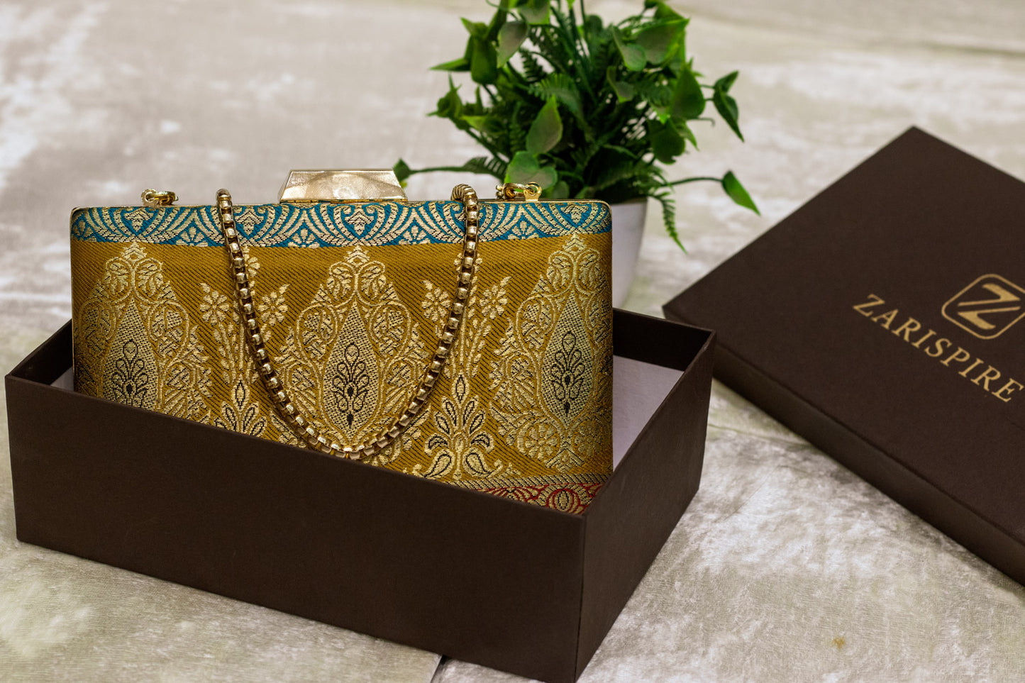Traditional handmade Banarasi brocade clutch bag in gold and turquoise with intricate patterns and a gold chain strap.