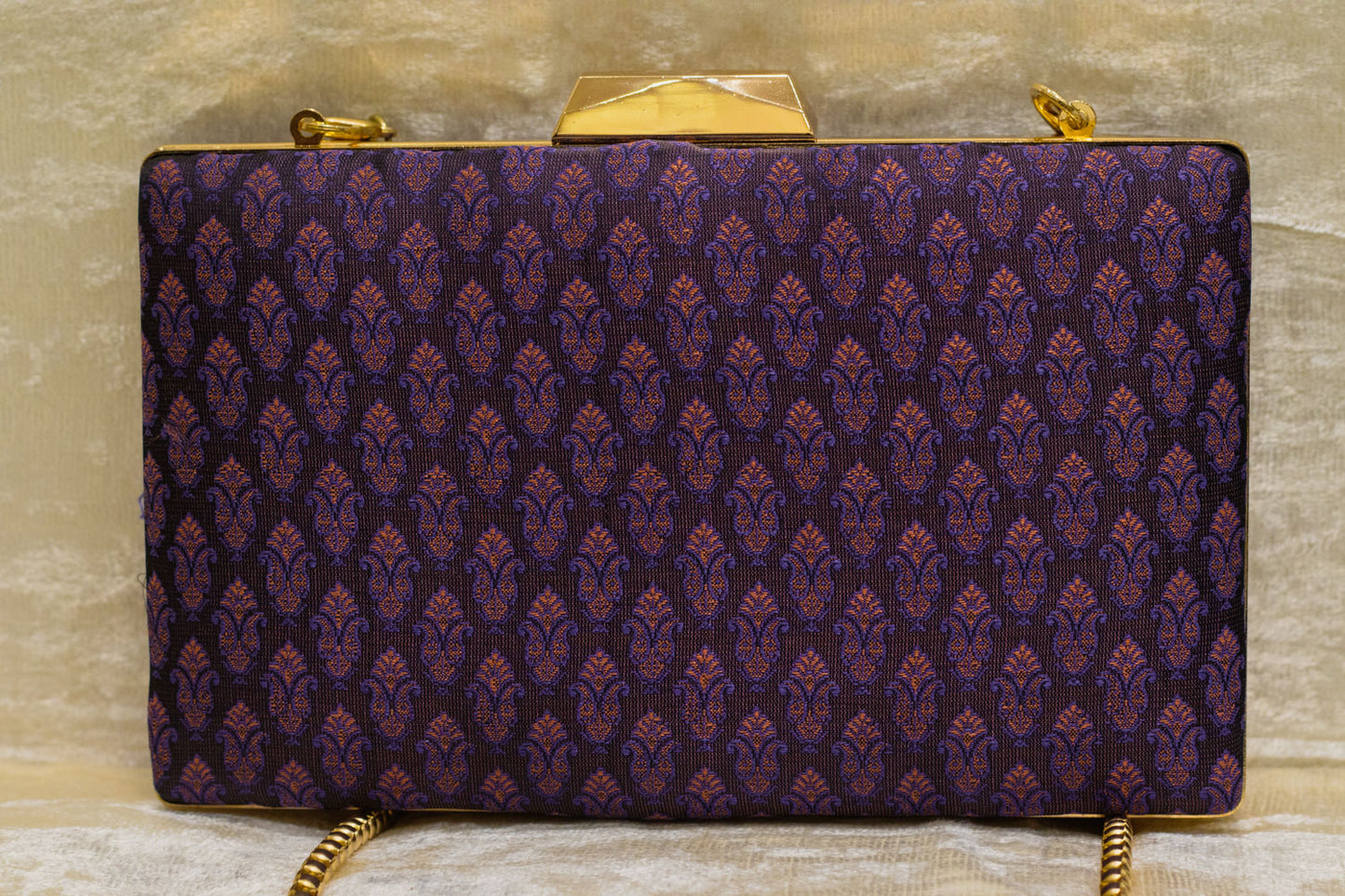 Plum Banarasi brocade clutch bag with traditional handmade pattern and gold-tone clasp and chain.