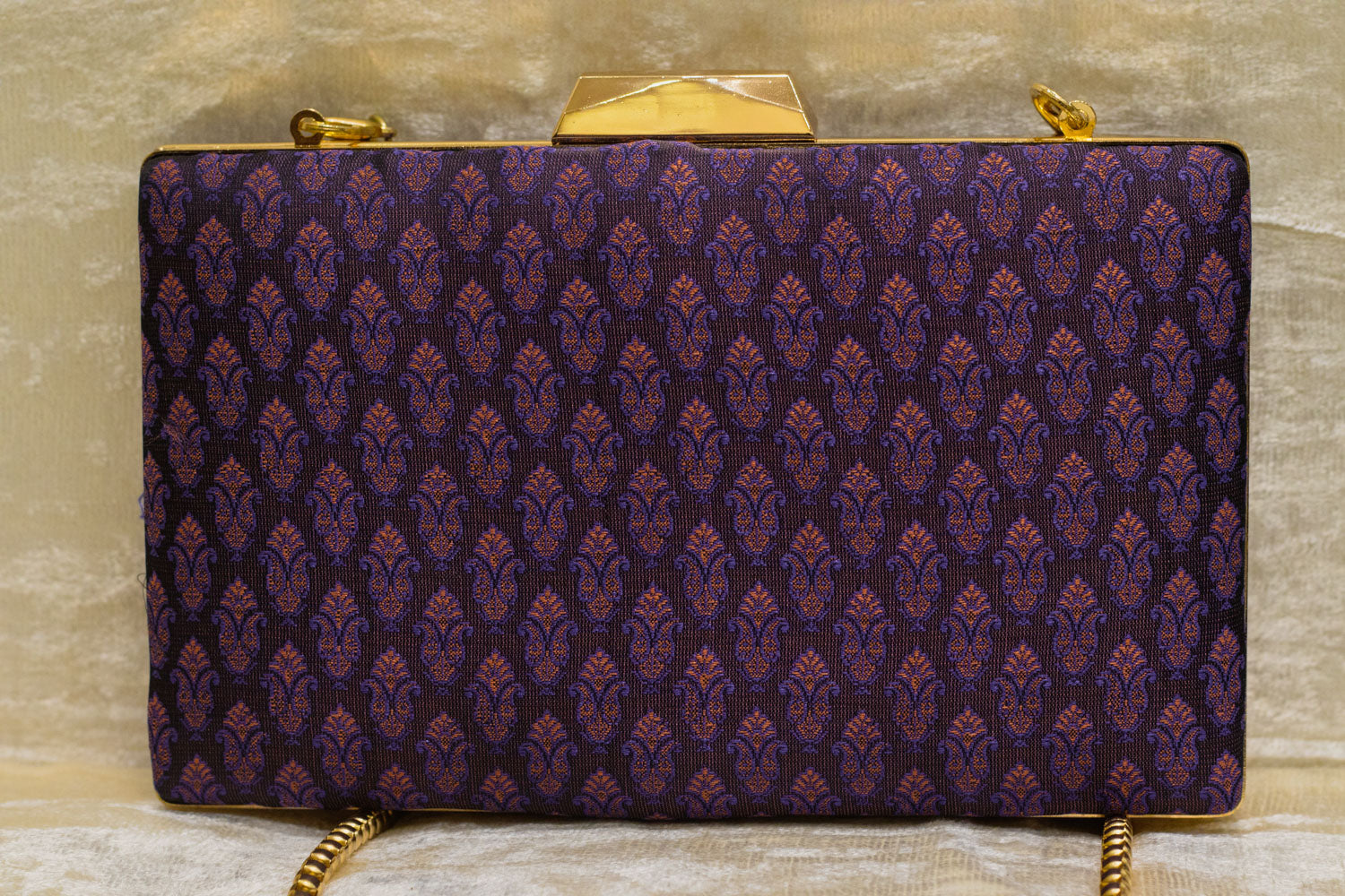 Plum Banarasi brocade clutch bag with traditional handmade pattern and gold-tone clasp and chain.