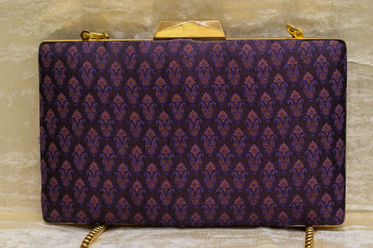 Plum Banarasi brocade clutch bag with traditional handmade pattern and gold-tone clasp and chain.