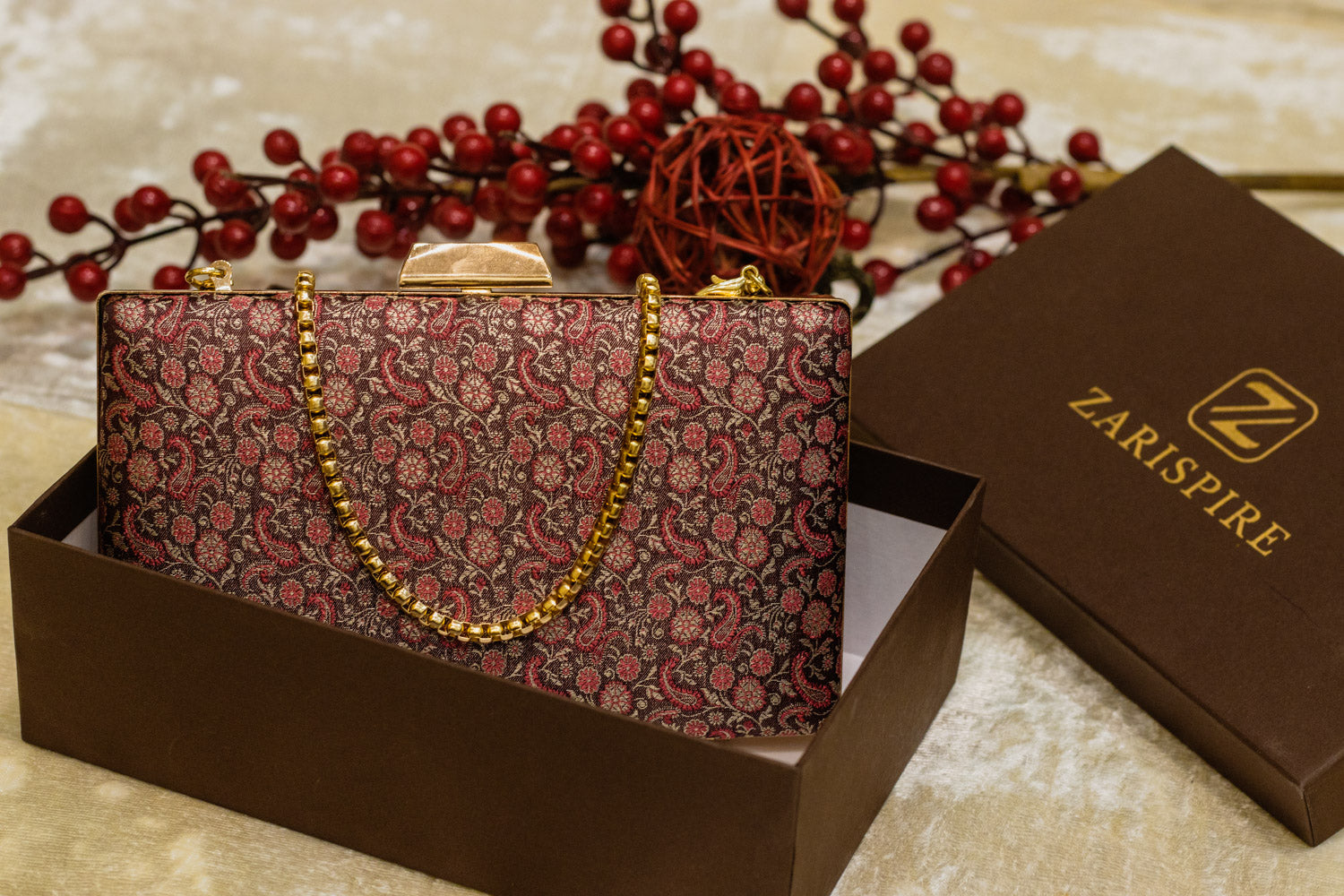 Wine-colored Banarasi brocade clutch bag with intricate floral patterns and gold chain, traditional handmade design.