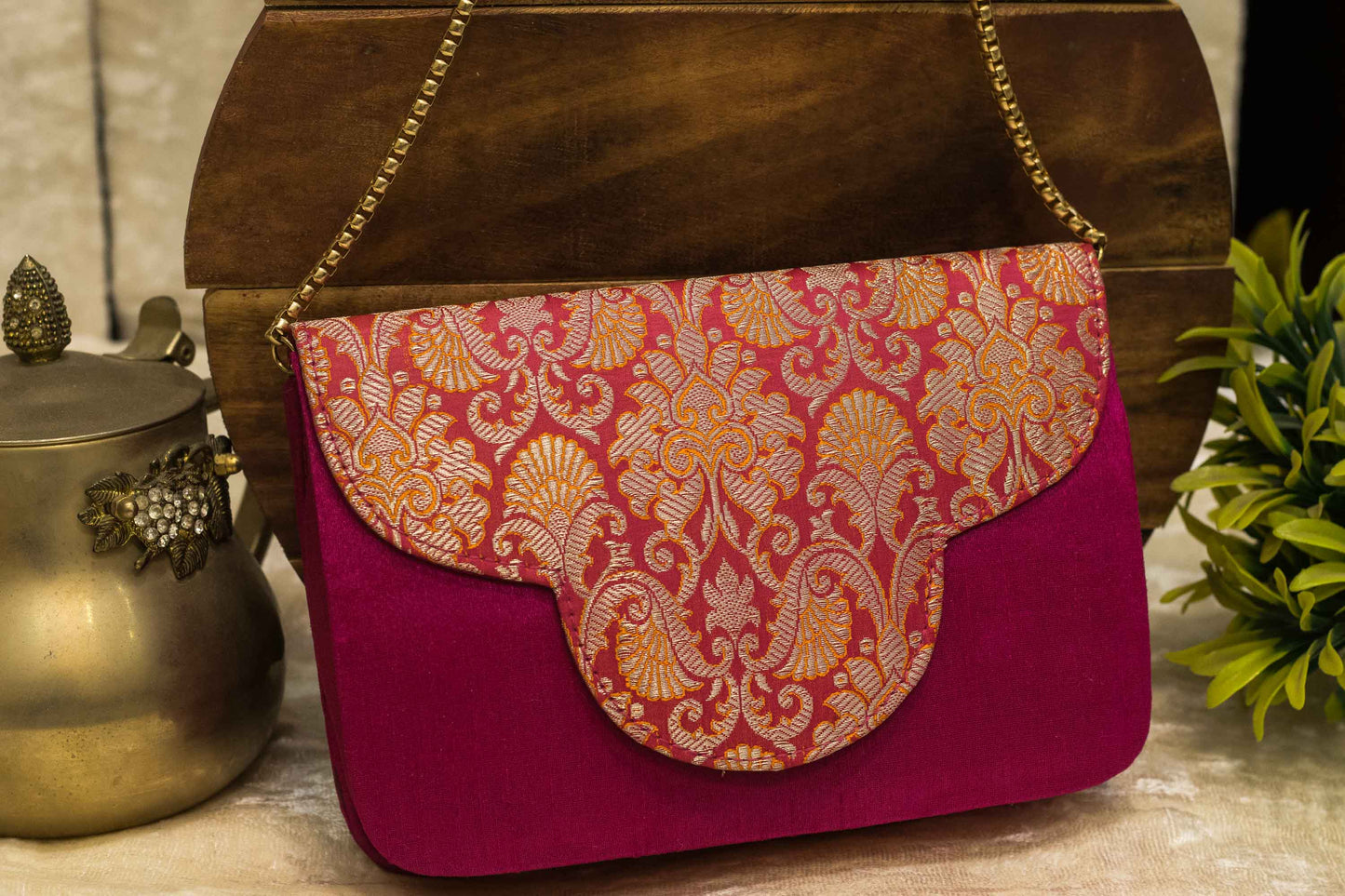 Traditional handmade brocade Banarasi clutch bag in vibrant rani pink with gold floral patterns and a gold chain strap.