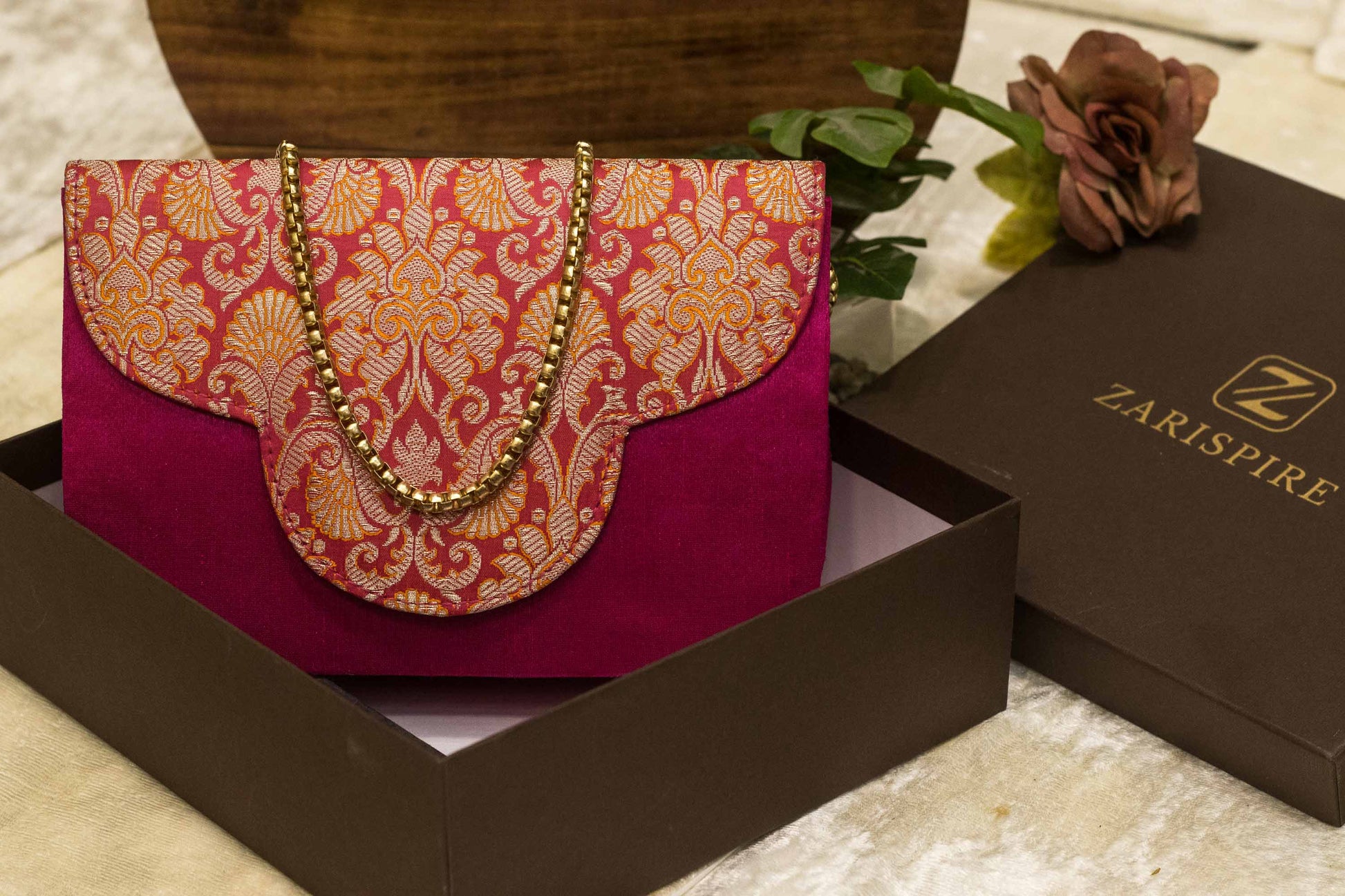 Traditional handmade Banarasi brocade clutch bag in rich rani pink with gold floral patterns and chain strap.